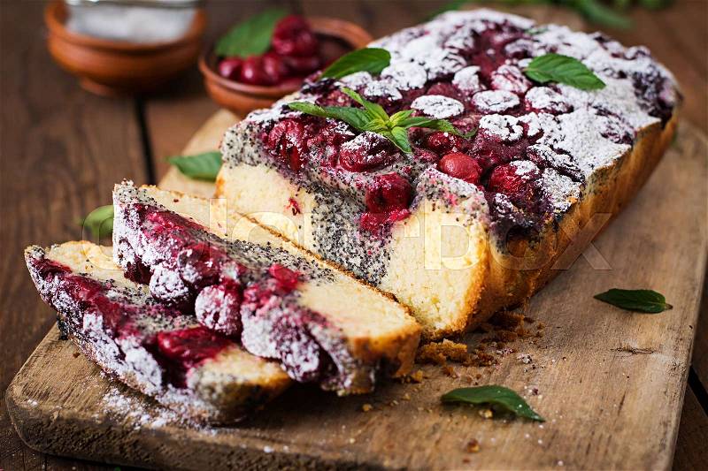 Cherry poppy seed cake dusted with powdered sugar on a wooden table, stock photo