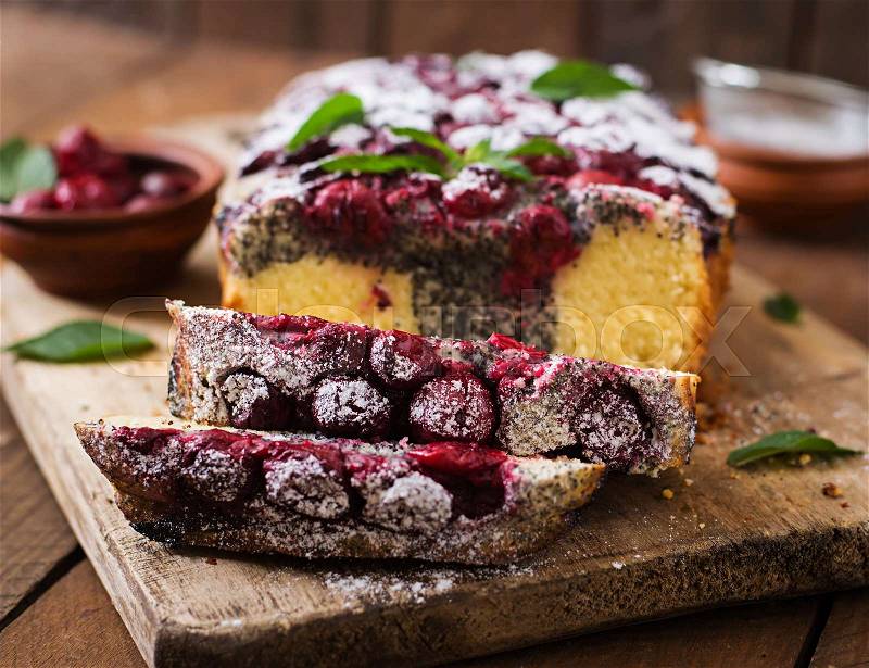 Cherry poppy seed cake dusted with powdered sugar on a wooden table, stock photo
