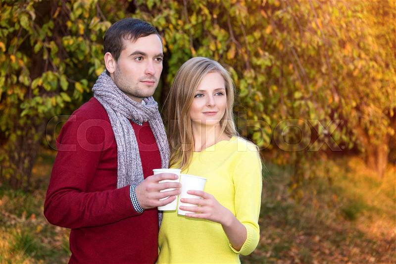 Love, relationship, season, friendship and people concept - happy man and woman enjoying golden autumn fall season with paper coffee cups in the park. Young couple drinking hot cofee or tea, stock photo