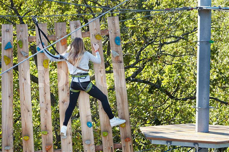 Girl athlete runs an obstacle course in climbing amusement park, stock photo