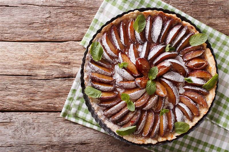 Sweet plum tart with mint and powdered sugar close-up on the table. Horizontal view from above , stock photo