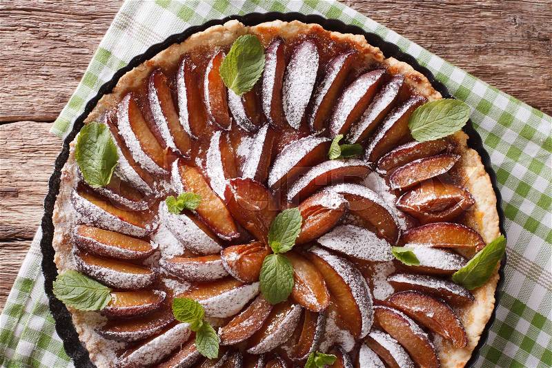 Delicious pastry: plum tart with mint and powdered sugar close-up on the table. Horizontal view from above , stock photo