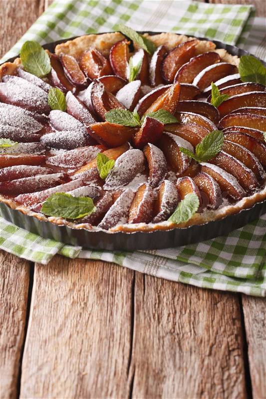 Sweet plum tart with mint and powdered sugar close-up on the table. vertical\, stock photo