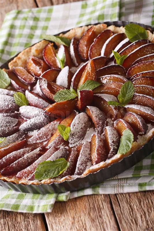 Freshly baked plum tart decorated with mint and powdered sugar close-up on the table. Vertical\, stock photo