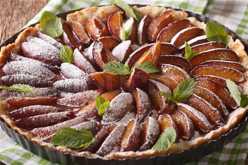 Freshly baked plum tart decorated with mint and powdered sugar close-up on the table. horizontal , stock photo