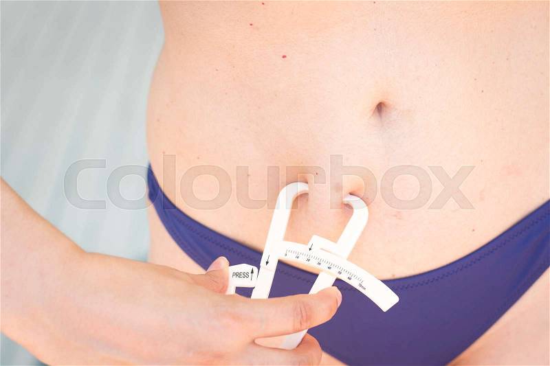 Slim attractive young lady wearing bikini in summer using fat caliper to measure bodyfat, stock photo