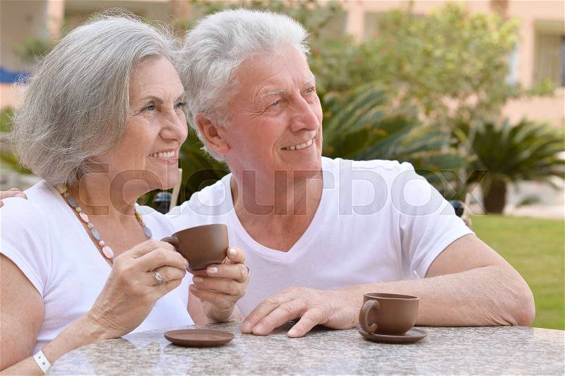 Loving senior couple sitting with coffee in tropical resort, stock photo