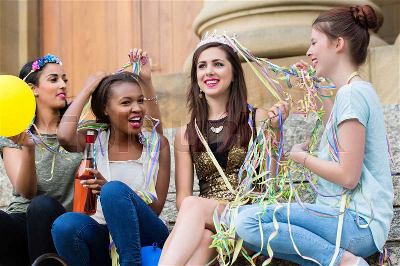 Friends decorate the bride with paper streamers, sitting, in front of pillar on bachelorette party, stock photo