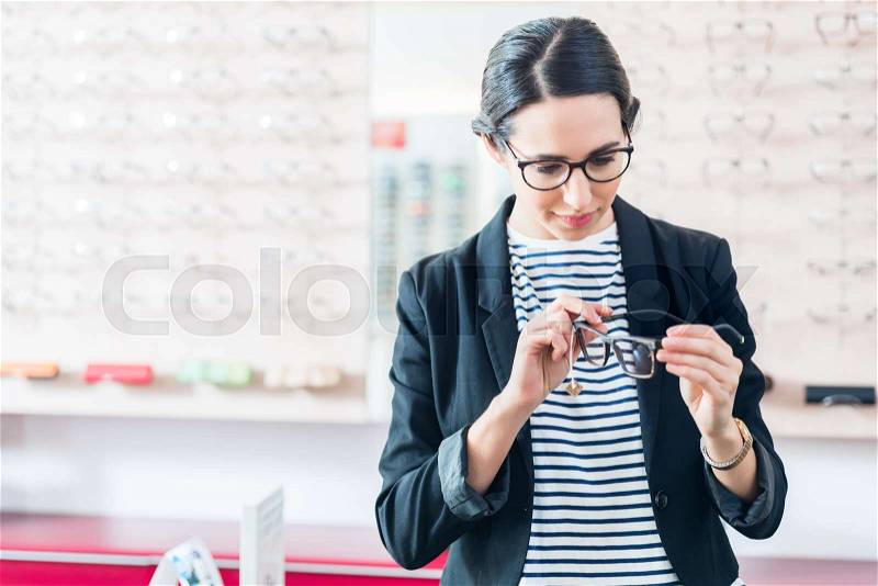 Woman taking glasses off shelf in optician shop, stock photo