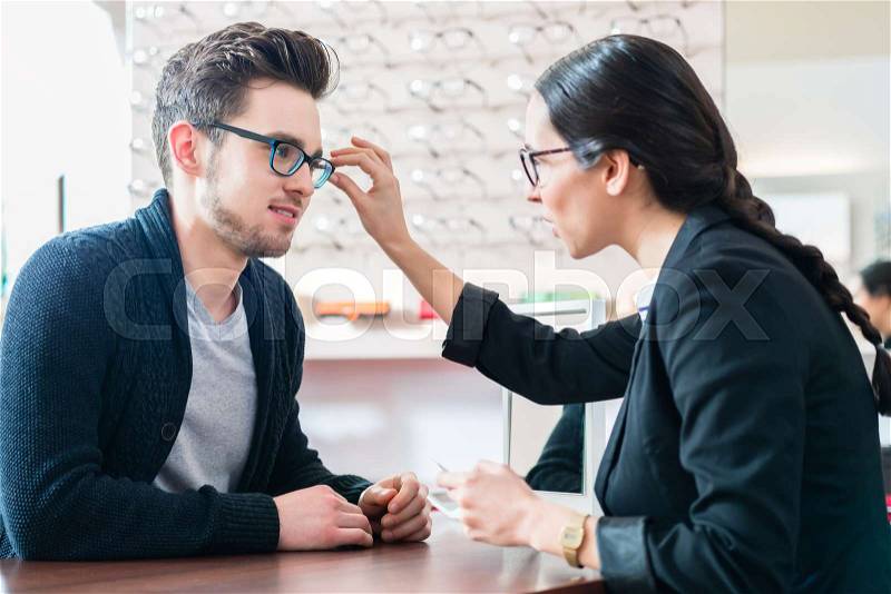 Man in optician shop getting advice from saleswoman buying new glasses, stock photo