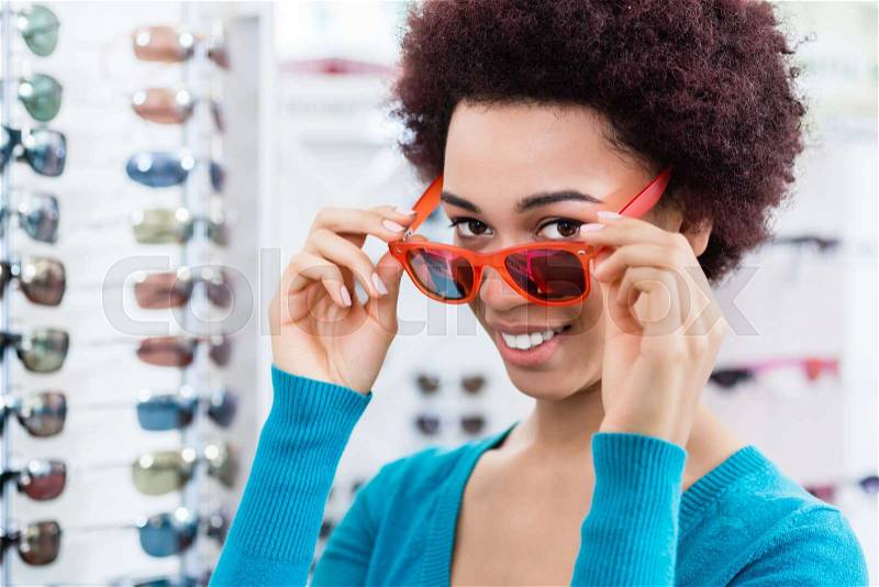 Black woman wearing and buying sunglasses in optician shop, stock photo