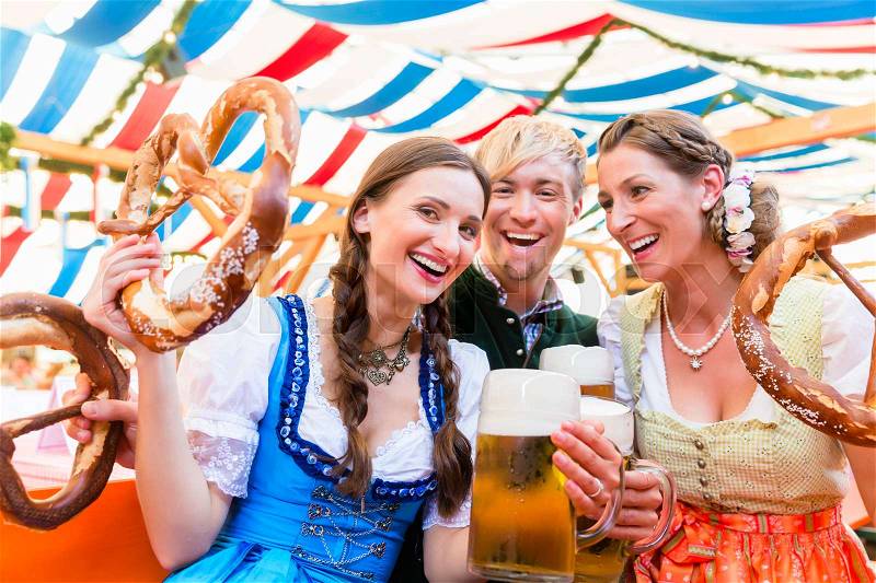 Three friends in beer tent at Dult or Oktoberfest holding giant pretzels up in the air, stock photo