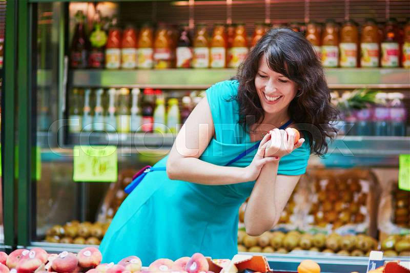 Beautiful French woman choosing ripe organic peaches on a Parisian local market. Customer in food store, supermarket or hypermarket concept, stock photo