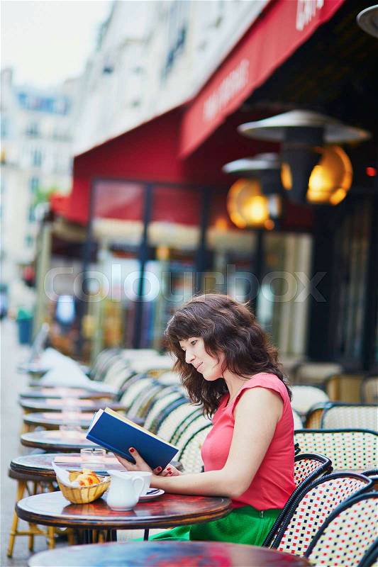 Beautiful young woman drinking coffee and reading a book in Parisian outdoor cafe. Student preparing for exam in Paris. International education exchange program in France concept, stock photo