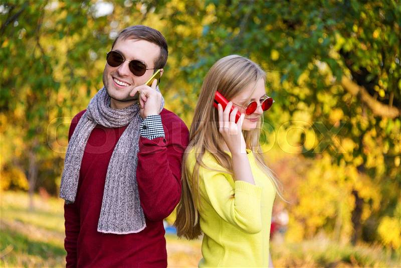 Young couple using a mobile phones. Young couple talking themselves by mobile phone in the autumn park, stock photo