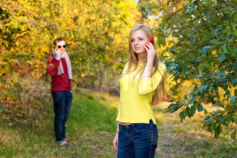 Young couple using a mobile phones. Young couple talking themselves by mobile phone in the autumn park, stock photo