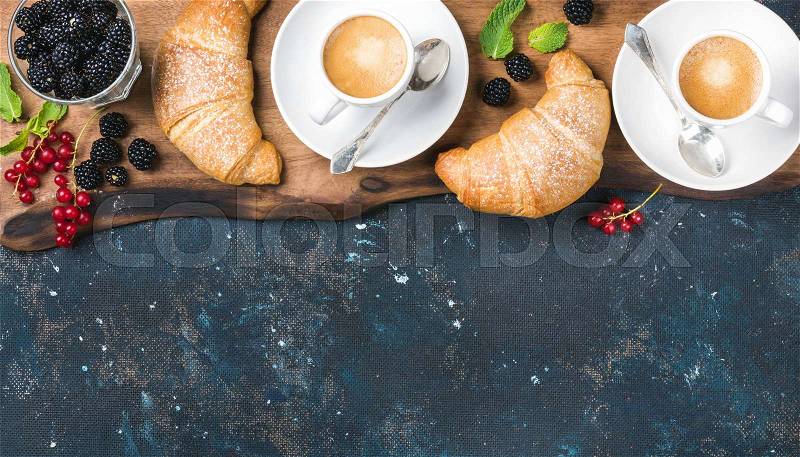 Breakfast set. Freshly baked croissants with garden berries and coffee cups on rustic wooden board over dark grunge plywood backdrop, top view, copy space, stock photo