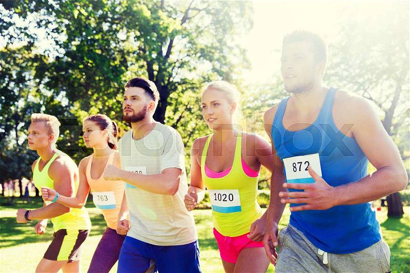Fitness, sport, race and healthy lifestyle concept - group of happy teenage friends or sportsmen running marathon with badge numbers outdoors, stock photo