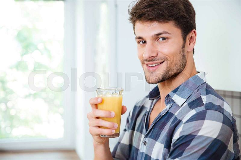 Smiling young man in plaid shirt drinking fresh juice on the kitchen, stock photo