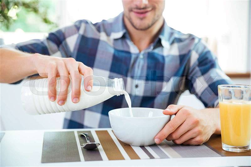 Man pouring milk into bowl for breakfast on the kitchen, stock photo