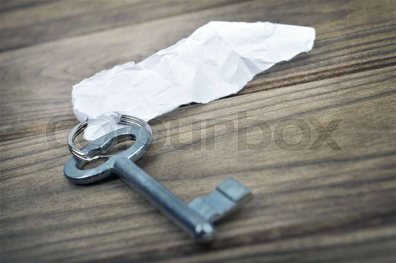 Closeup of key with empty note on wooden table, stock photo