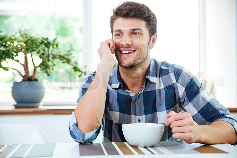 Happy man using smartphone and having breakfast on the kitchen, stock photo