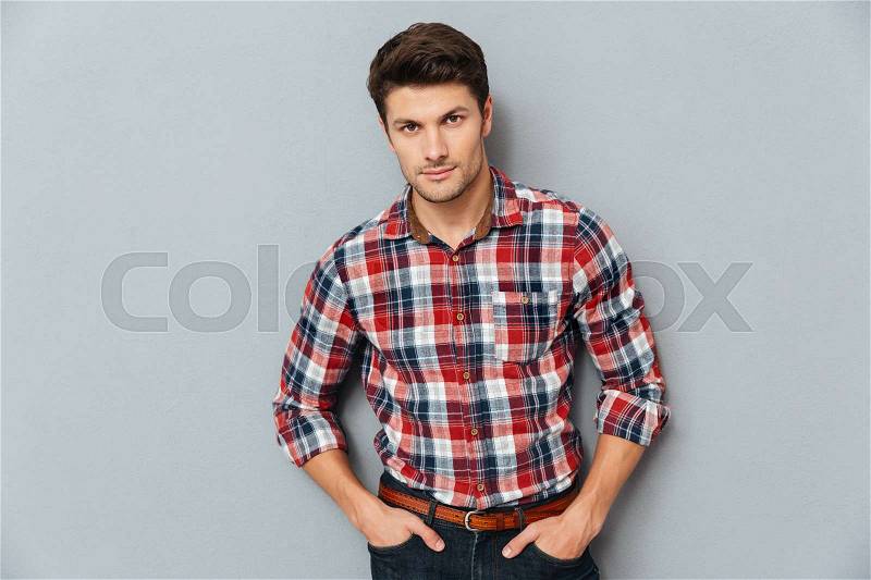Handsome young man standing with hands in pockets over gray background, stock photo
