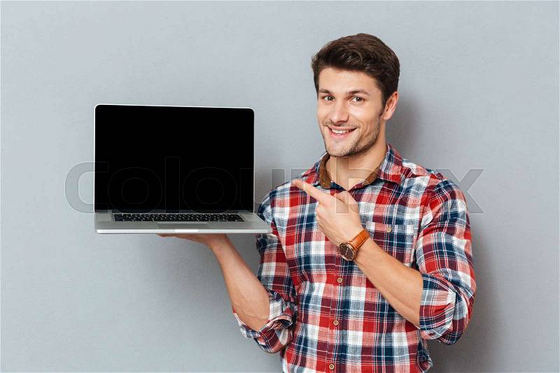 Happy young man in plaid shirt pointing on blank screen laptop, stock photo