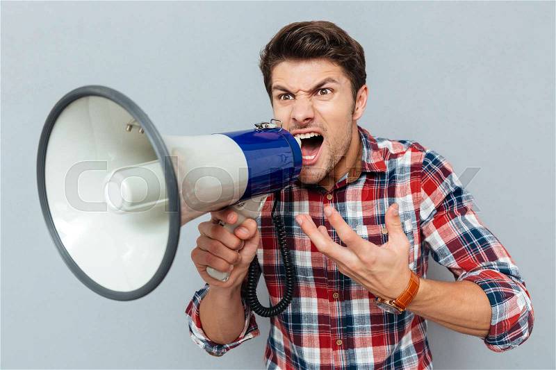 Portrait of a man screaming in megaphone isolated on a gray background, stock photo