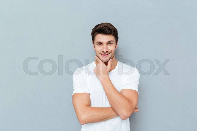 Handsome young smiling pensive man standing and looking up isolated on the gray background, stock photo