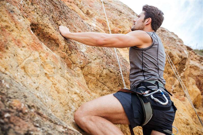 Young fearless man climbing a steep wall in mountain, stock photo
