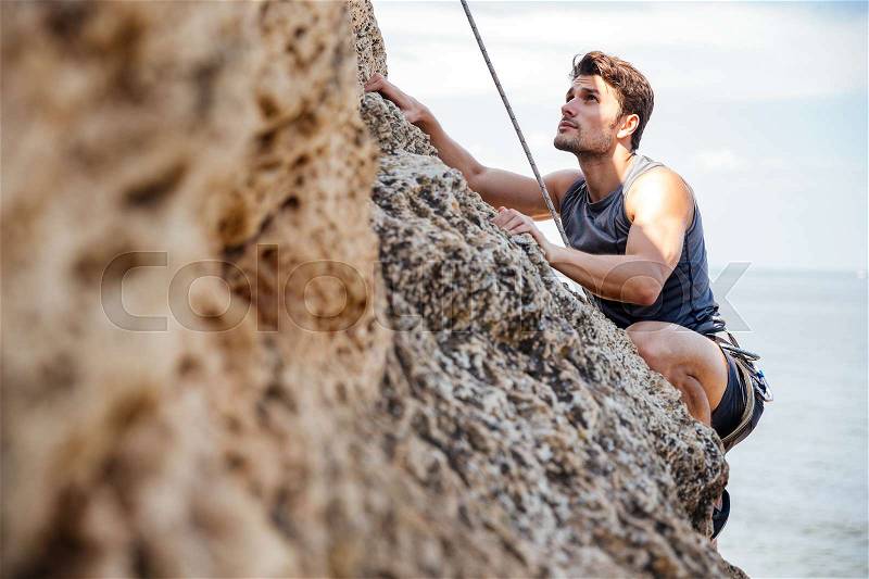 Young brunette man climbing natural rocky wall, stock photo