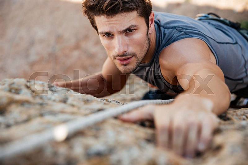 Man reaching for a grip while he rock climbs on a steep cliff, stock photo