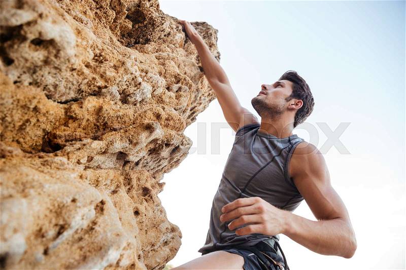 Man reaching for a grip while he rock climbs on a steep cliff, stock photo