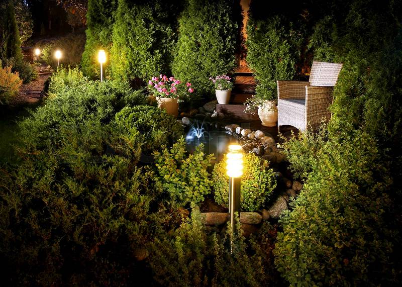 Illuminated home garden patio plants and evening lights near small fountain, stock photo