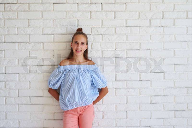 Happy girl standing with her hands behind her back, wearing casual outfit against white background, stock photo
