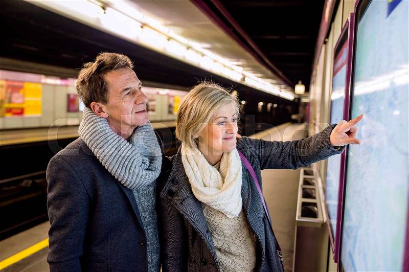 Beautiful senior couple standing at the underground platform, waiting, looking at the map, stock photo