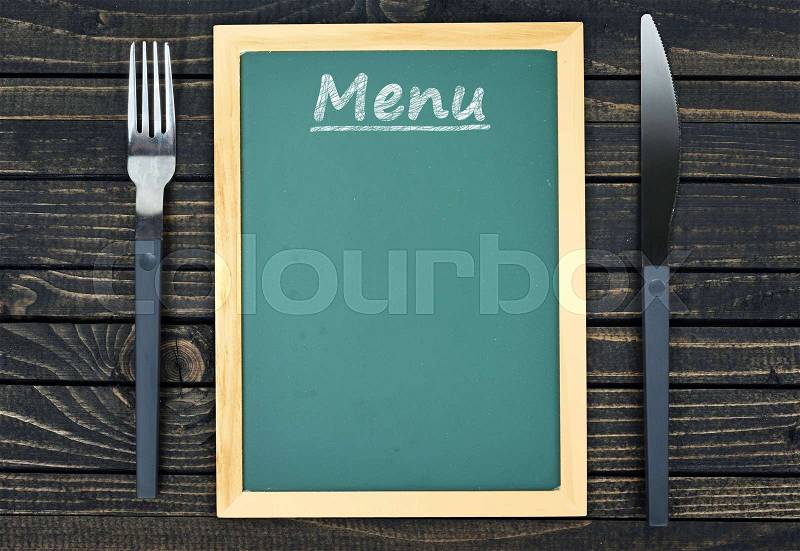 Fork and knife with menu on wooden table, stock photo