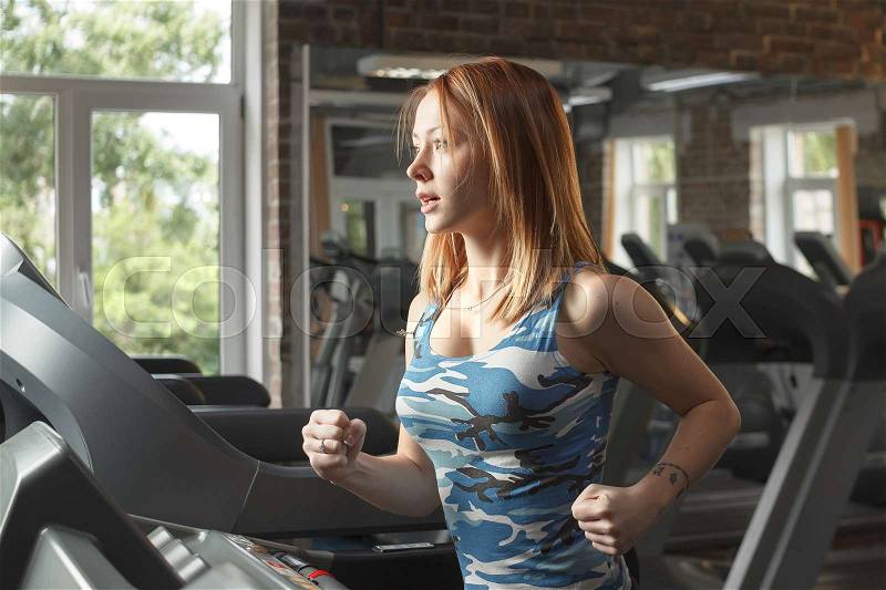 Concept: sport, healthy lifestyle. Young strong girl running on treadmill in gym, stock photo