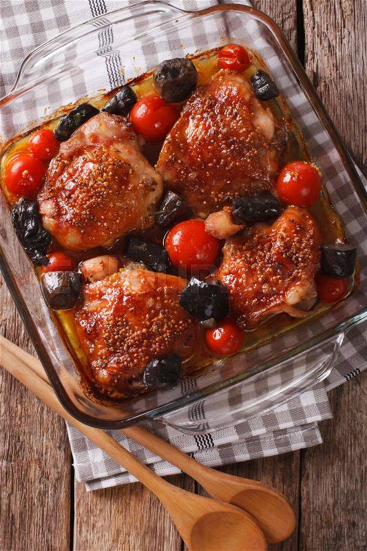 Baked chicken thigh with mustard, tomatoes and wild mushrooms close up in baking dish on the table. vertical view from above\, stock photo