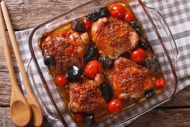 Baked chicken thigh with mustard, tomatoes and wild mushrooms close up in baking dish on the table. horizontal view from above , stock photo