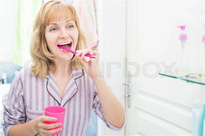 Pretty young female looking in mirror while brushing teeth in bathroom. Happy woman cleaning her oral cavity caring about dental health, stock photo