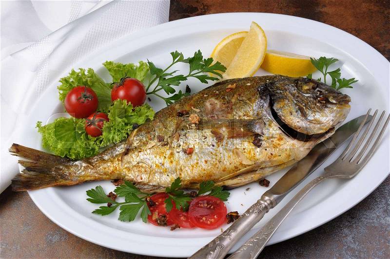 Roasted fish Dorado with vegetables garnish and lemon slices on a plate, stock photo