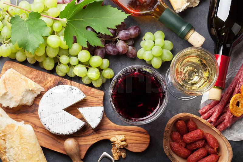 Red and white wine, grape, cheese and sausages on stone table. Top view, stock photo
