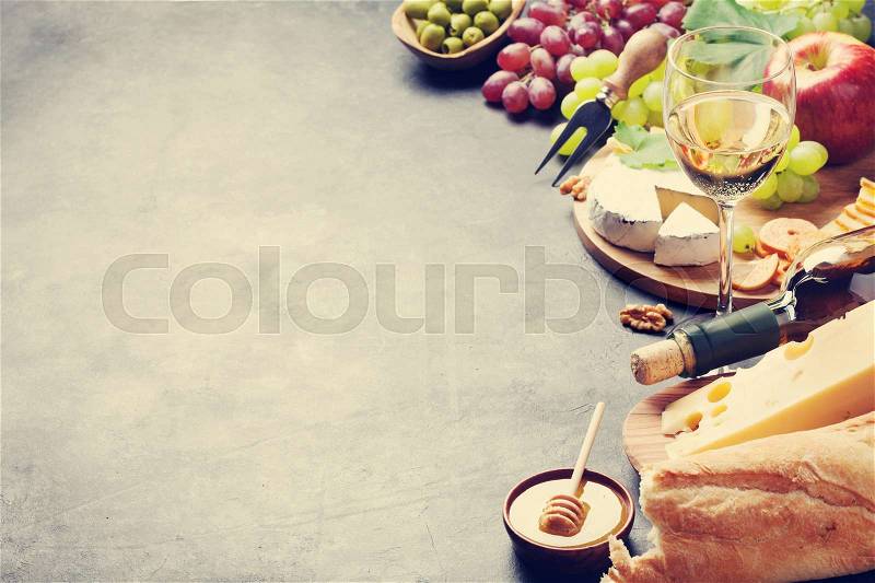 White wine, grape, bread, cheese plate and honey on stone table. View with copy space. Toned, stock photo