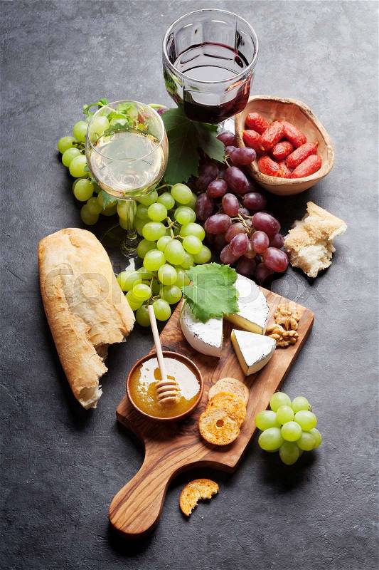 Red and white wine, grape, cheese and sausages on stone table, stock photo