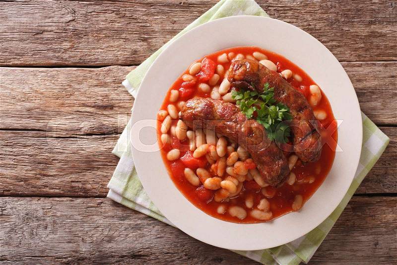 Grilled sausage with beans in tomato sauce on a plate close-up on the table. horizontal view from above , stock photo