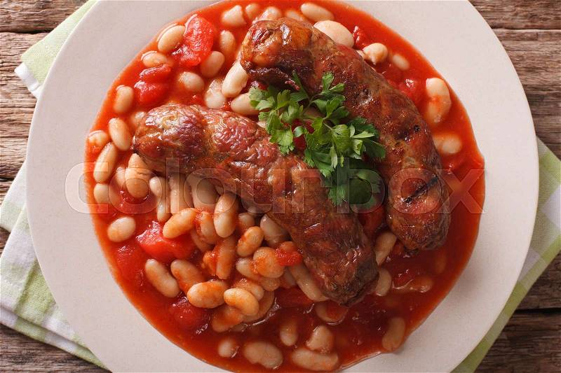 Pork sausages with beans and cooked tomatoes on a plate close-up on the table. horizontal view from above , stock photo