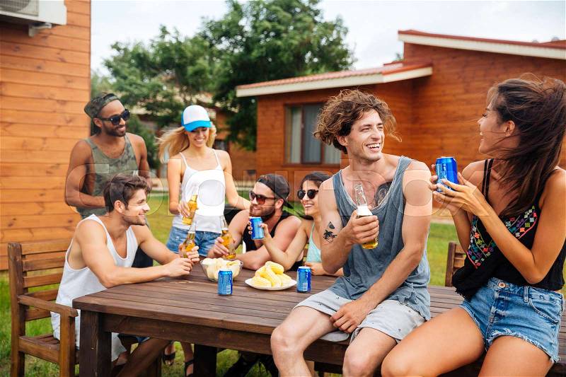 Cheerful young couple drinking beer and soda with friends on outdoor summer party, stock photo