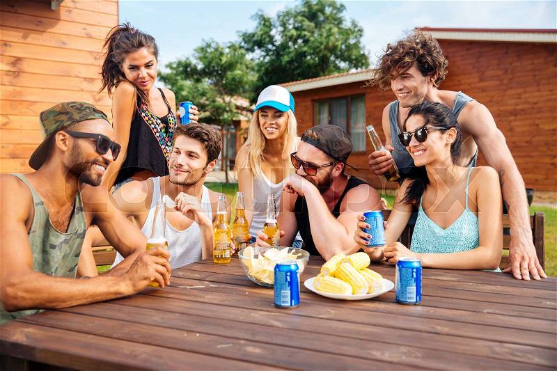 Portrait of cheerful young friends laughing and having party at the table outdoors, stock photo